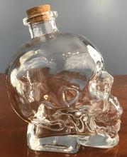 profile view of an empty glass skull drinks decanter with a cork lid displayed on a wooden table
